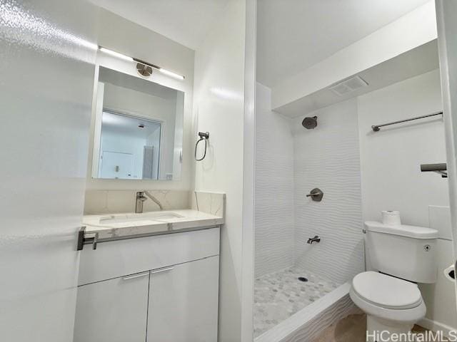 full bathroom with a tile shower, baseboards, toilet, and vanity