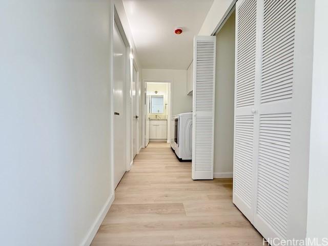 corridor featuring washer / dryer, light wood finished floors, and baseboards