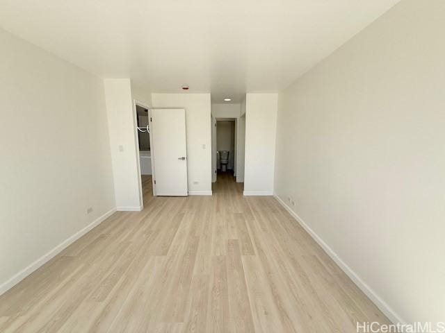 unfurnished bedroom with a walk in closet, a closet, light wood finished floors, and baseboards