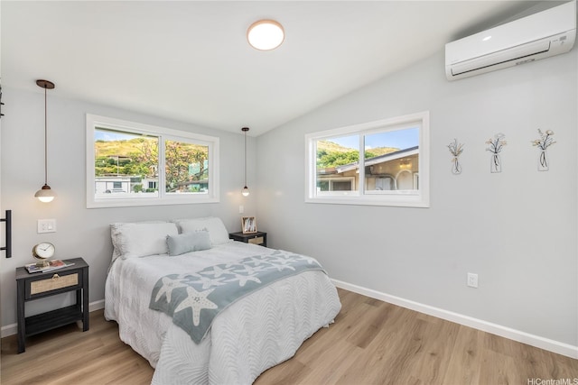 bedroom featuring an AC wall unit, lofted ceiling, light wood finished floors, and baseboards