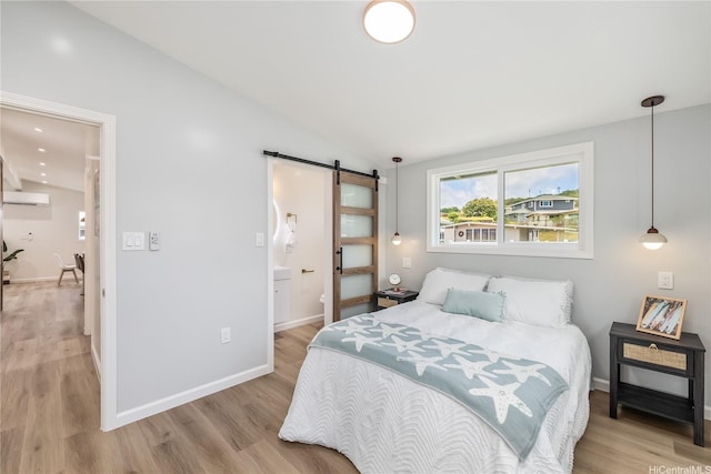 bedroom with a barn door, lofted ceiling, light wood finished floors, and a wall mounted air conditioner