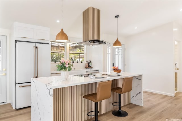kitchen featuring white cabinets, light wood finished floors, a kitchen breakfast bar, high end white fridge, and island range hood