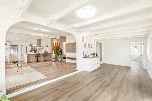 living area with arched walkways, light wood-style flooring, and plenty of natural light