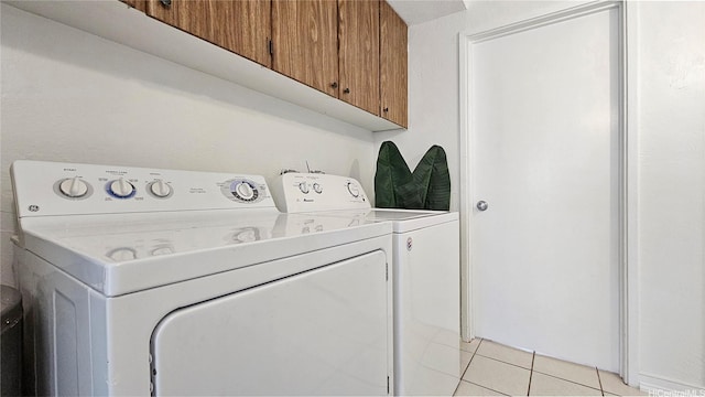 clothes washing area featuring washing machine and dryer, cabinet space, and light tile patterned floors
