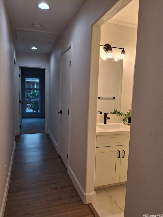 hall featuring attic access, a sink, light wood-type flooring, baseboards, and recessed lighting