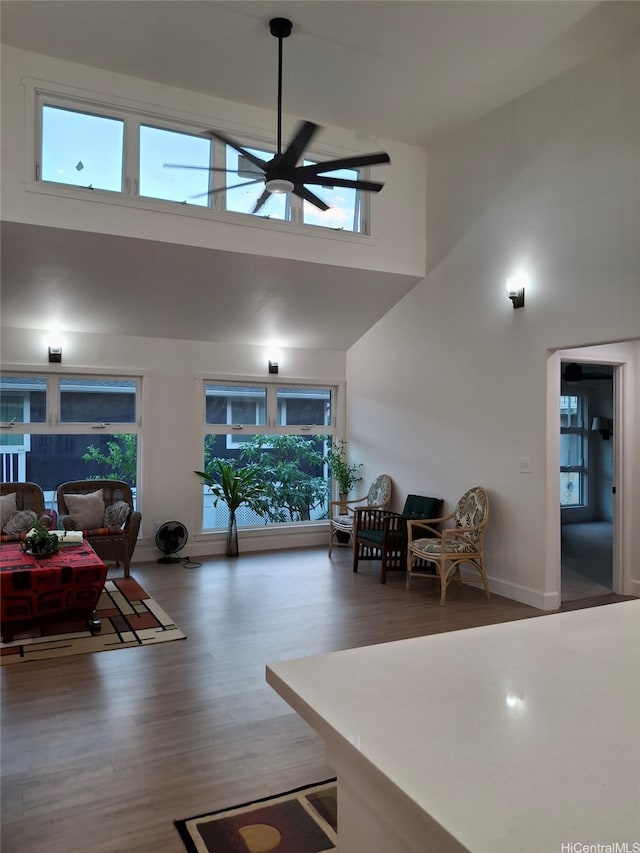 living room featuring a high ceiling, a ceiling fan, wood finished floors, and baseboards