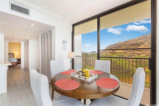 dining space featuring light wood-type flooring, a wall of windows, visible vents, and a mountain view