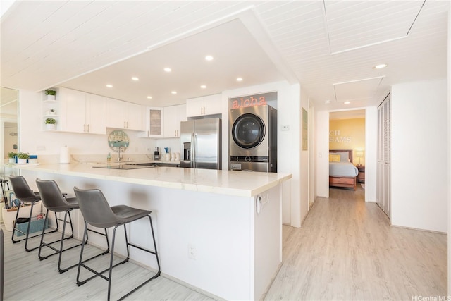 kitchen featuring stainless steel refrigerator with ice dispenser, a peninsula, stacked washing maching and dryer, and light wood-style floors