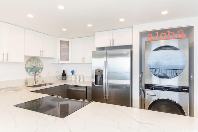 kitchen featuring a sink, stacked washer / drying machine, stainless steel appliances, light stone countertops, and recessed lighting
