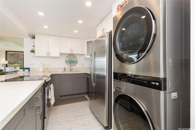 clothes washing area featuring light wood finished floors, a sink, recessed lighting, stacked washer / dryer, and laundry area