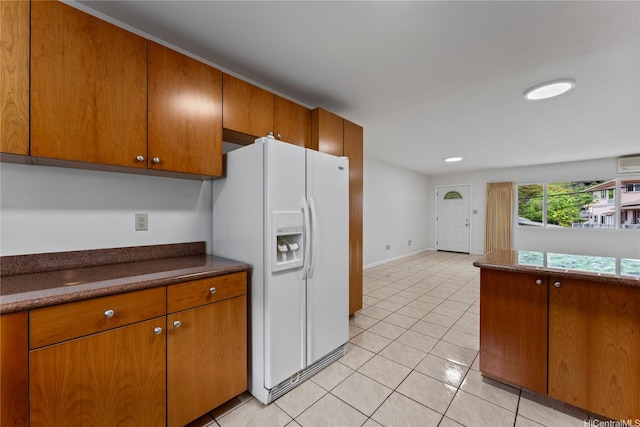 kitchen with brown cabinetry, dark countertops, baseboards, white refrigerator with ice dispenser, and light tile patterned floors