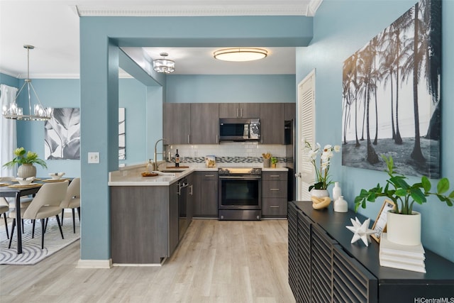 kitchen featuring appliances with stainless steel finishes, light countertops, a chandelier, tasteful backsplash, and light wood finished floors