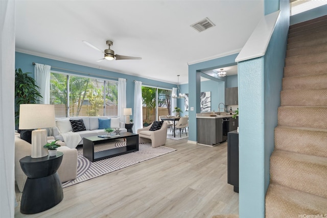 living room with light wood-type flooring, stairway, crown molding, a ceiling fan, and a chandelier