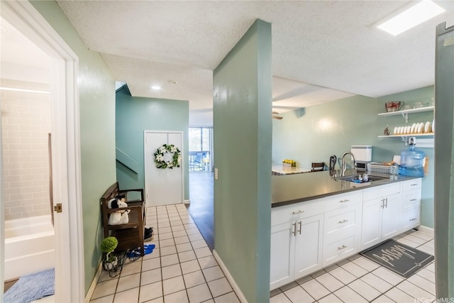 kitchen with open shelves, white cabinets, a sink, a textured ceiling, and light tile patterned flooring