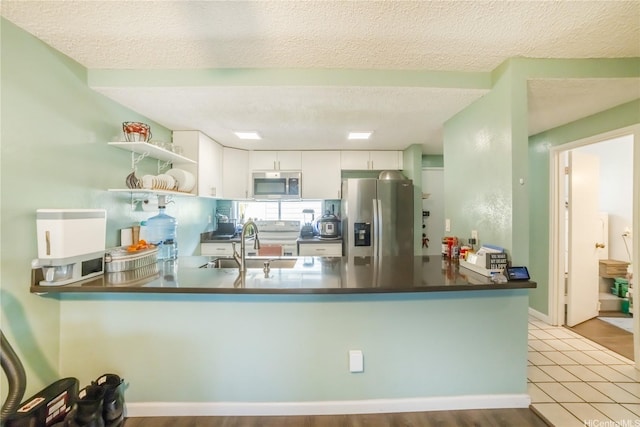 kitchen with a sink, a peninsula, white cabinetry, dark countertops, and appliances with stainless steel finishes