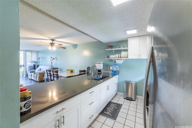 kitchen with a sink, light tile patterned floors, white cabinetry, dark countertops, and freestanding refrigerator