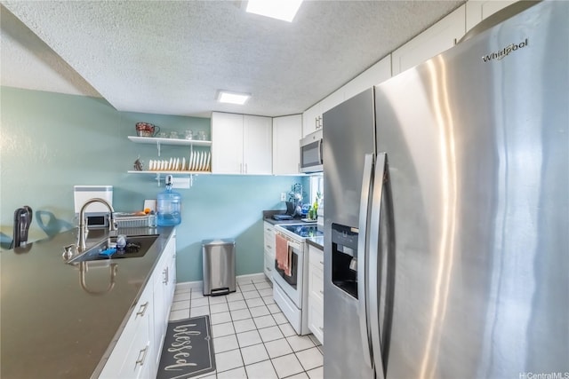 kitchen featuring a sink, stainless steel appliances, light tile patterned flooring, white cabinetry, and a textured ceiling