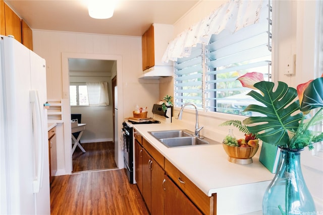 kitchen with brown cabinets, wood finished floors, a sink, freestanding refrigerator, and black gas range