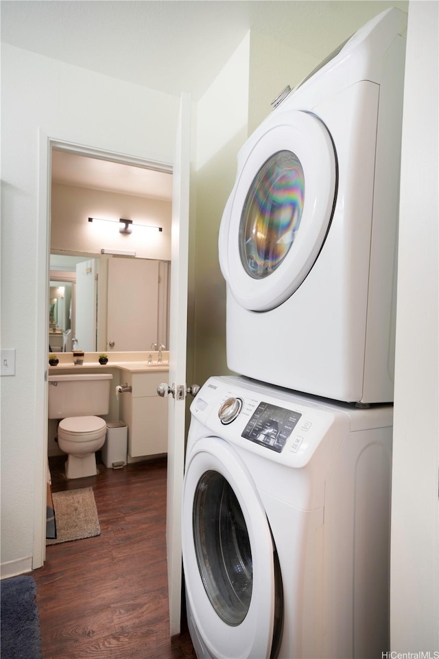clothes washing area with wood finished floors, stacked washer / dryer, laundry area, and a sink