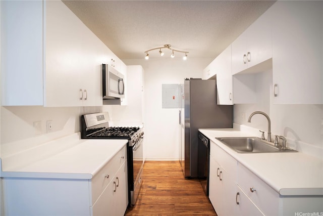 kitchen with white cabinets, light countertops, wood finished floors, a sink, and appliances with stainless steel finishes