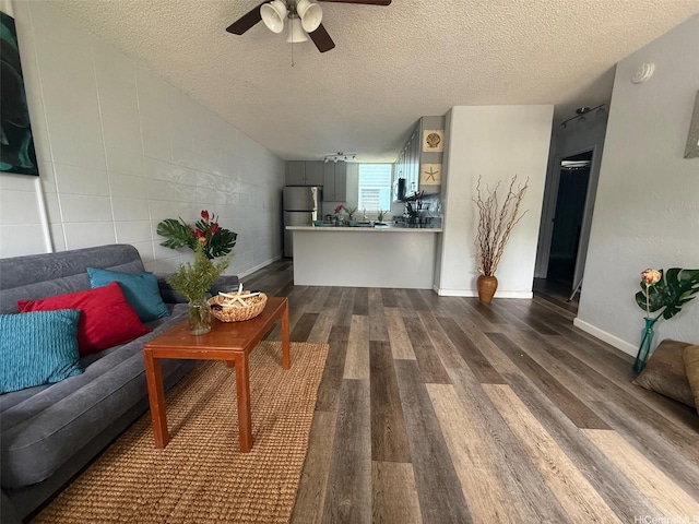 living room featuring baseboards, a ceiling fan, dark wood-style flooring, and a textured ceiling