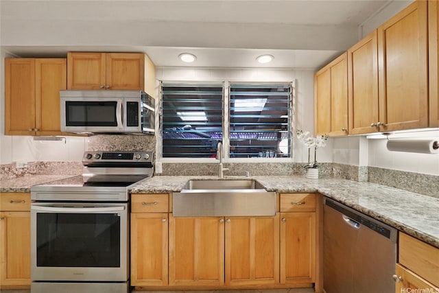 kitchen with light stone counters, light brown cabinets, stainless steel appliances, and a sink