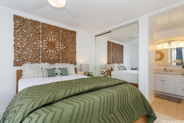 bedroom featuring light wood-style floors, a closet, ensuite bath, and a sink