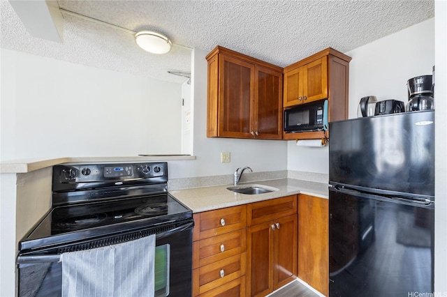 kitchen with black appliances, a textured ceiling, light countertops, and a sink