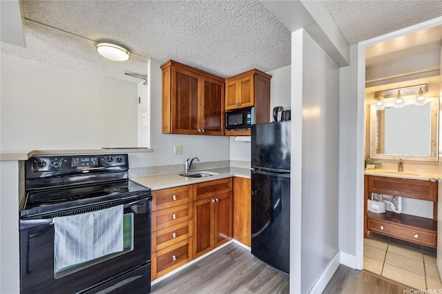 kitchen featuring black appliances, a textured ceiling, a sink, and light countertops
