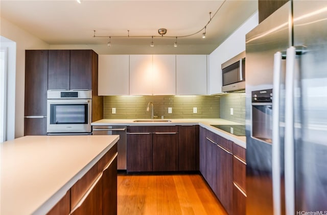 kitchen with a sink, light wood-type flooring, stainless steel appliances, light countertops, and backsplash