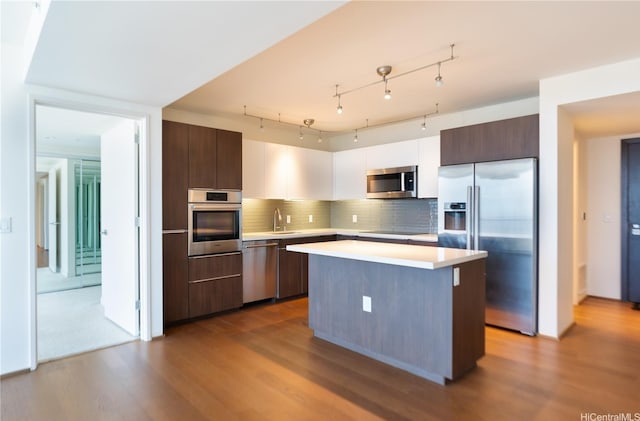kitchen featuring stainless steel appliances, light countertops, dark wood-type flooring, a center island, and tasteful backsplash
