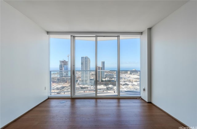 empty room with a wall of windows, a view of city, and hardwood / wood-style flooring