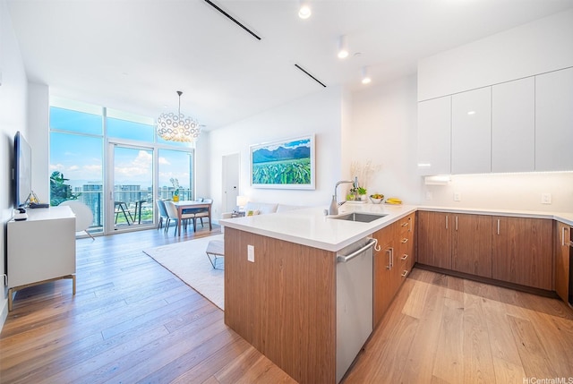 kitchen with a sink, a peninsula, light wood-style flooring, stainless steel dishwasher, and a notable chandelier