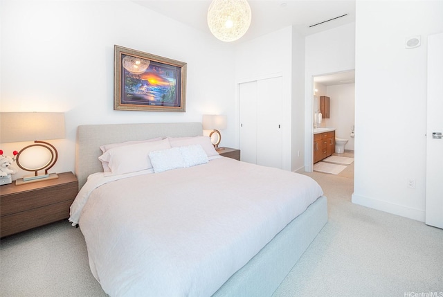 bedroom featuring baseboards, ensuite bathroom, light carpet, and a closet