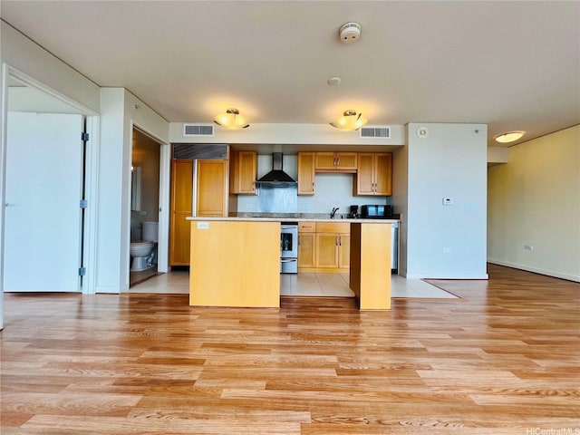 kitchen featuring wall chimney range hood, a center island, black microwave, light wood-type flooring, and visible vents