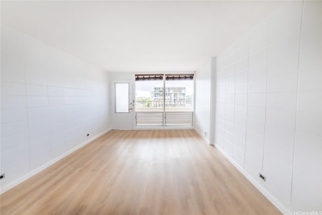 spare room featuring tile walls, light wood-style flooring, and baseboards