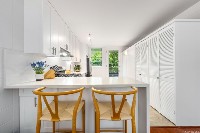 3131 Pualei Cir Unit 15, Honolulu, HI 96815 - kitchen featuring light countertops, stainless steel stove, under cabinet range hood, white cabinetry, and a kitchen bar