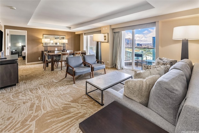 living area with a raised ceiling, baseboards, light colored carpet, and a city view