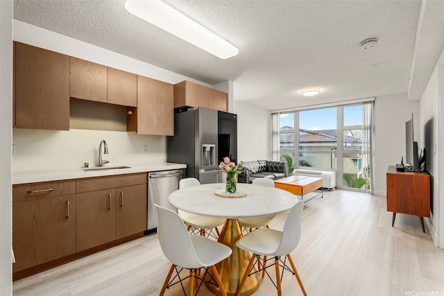 kitchen with a sink, a textured ceiling, light wood-style flooring, light countertops, and appliances with stainless steel finishes