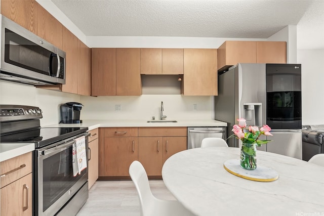 kitchen with stainless steel appliances, light countertops, a sink, and a textured ceiling