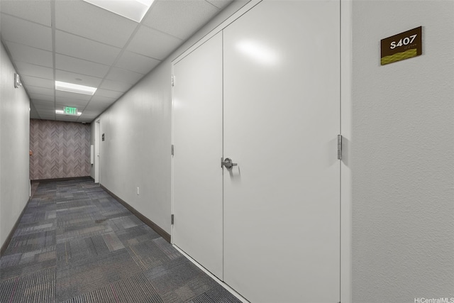 hall featuring dark colored carpet and a drop ceiling