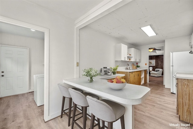 kitchen featuring a sink, freestanding refrigerator, light wood-style floors, light countertops, and a breakfast bar