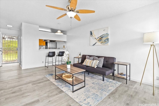 living room with a textured ceiling, ceiling fan, wood finished floors, and baseboards