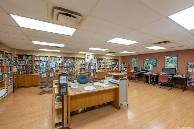 office space with light wood-type flooring, bookshelves, visible vents, and a drop ceiling