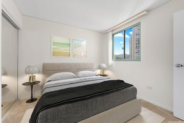 bedroom featuring light carpet, baseboards, a textured ceiling, and a closet