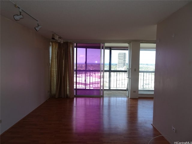 spare room with expansive windows, wood finished floors, and track lighting
