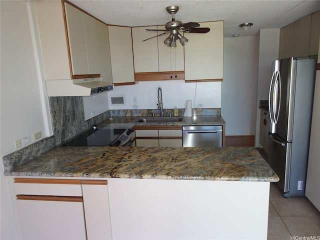 kitchen featuring a sink, ceiling fan, stone countertops, a peninsula, and appliances with stainless steel finishes