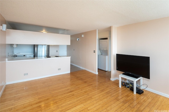 46-255 Kahuhipa St Unit A1204, Kaneohe, HI 96744 - unfurnished living room with a textured ceiling, a sink, light wood-style floors, baseboards, and stacked washer and clothes dryer