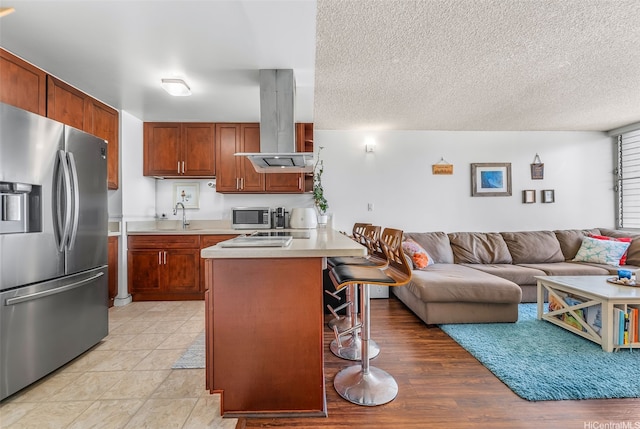kitchen with stainless steel appliances, island exhaust hood, a breakfast bar area, light countertops, and open floor plan