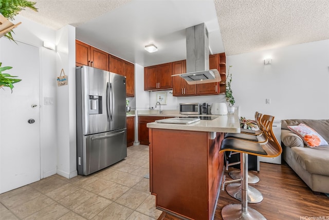 kitchen with island exhaust hood, a peninsula, light countertops, a textured ceiling, and appliances with stainless steel finishes